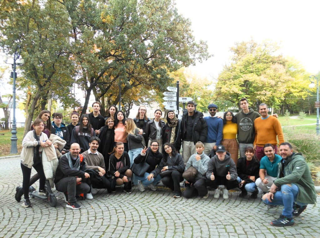 Group of students and adults posing together in a park on a cobblestone plaza with trees behind them in autumn colors.