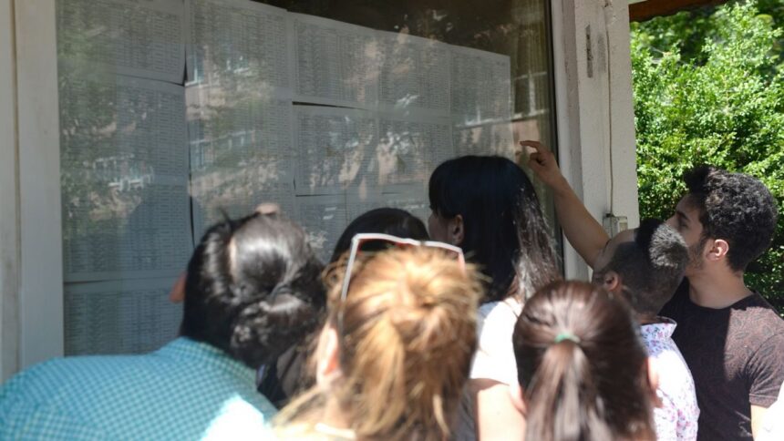 Group of people gathered around a glass bulletin board, reading posted schedules outside a building with greenery nearby.