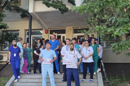 Group of healthcare workers in scrubs standing on building entrance stairs, holding flyers or posters for a blood drive or campaign.