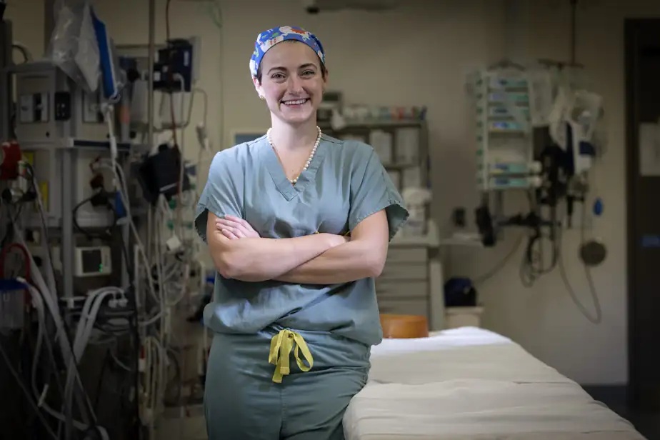 teodora dumitra - Jurnalul Olteniei – Știri din Craiova și Oltenia Female nurse in blue scrubs and a patterned cap stands with arms crossed in a hospital room filled with medical equipment.