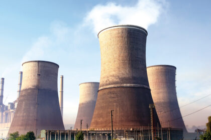 Massive concrete cooling towers at an industrial power plant with steam rising from the top.