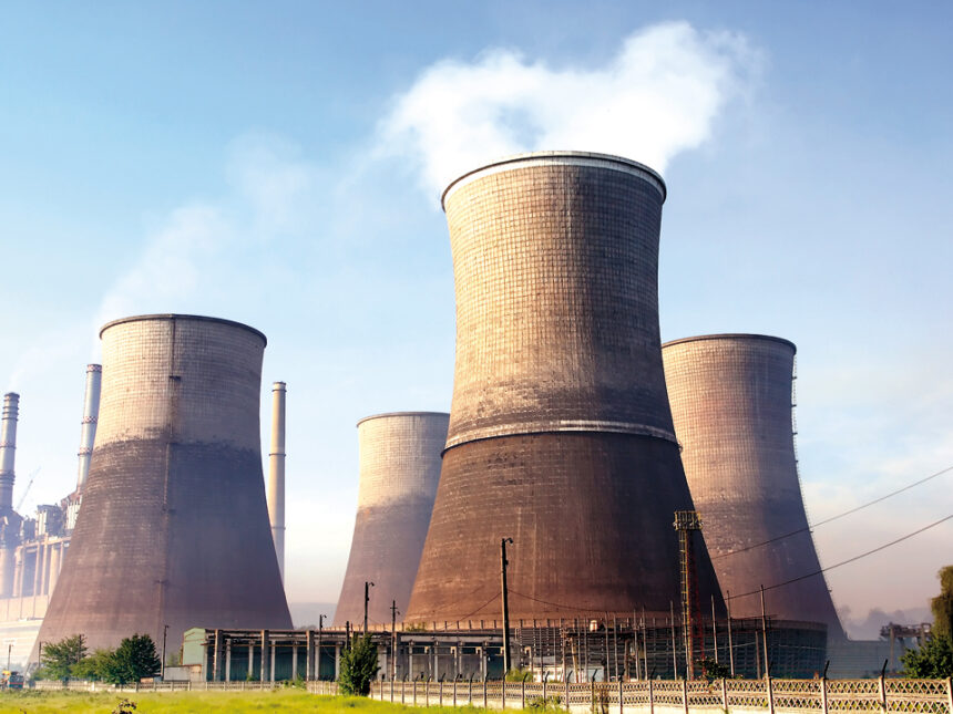 Massive concrete cooling towers at an industrial power plant with steam rising from the top.
