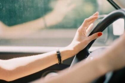 Close-up of a driver's hands on the steering wheel, with red nail polish and a bracelet visible in a car.