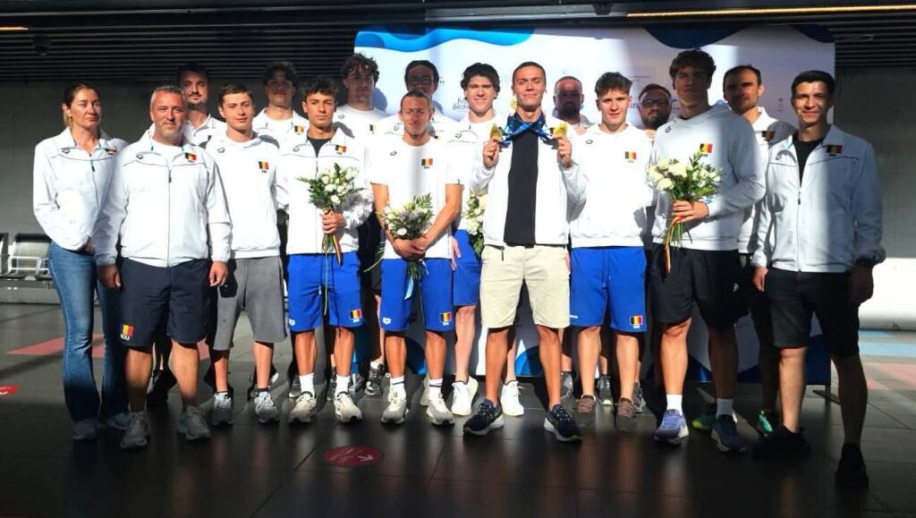 David Popovici. Foto: Facebook/FRNPM - Jurnalul Olteniei – Știri din Craiova și Oltenia Group of Belgian athletes in white jackets and blue shorts pose together, some holding bouquets and medals.