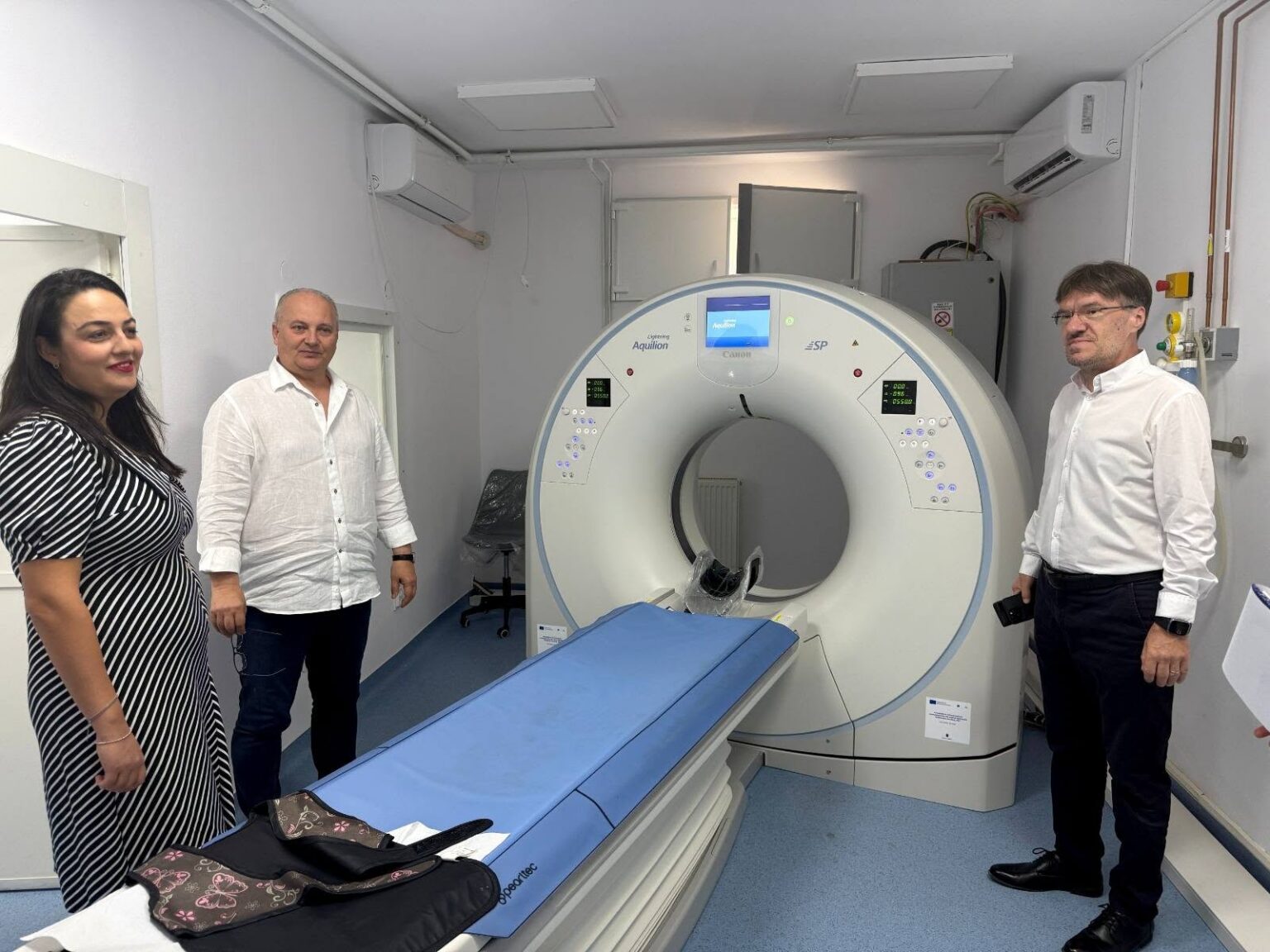 Three people stand beside a large MRI scanner in a clinical room.