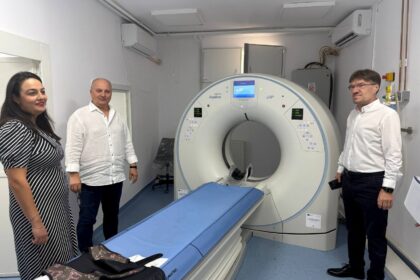 Three people stand beside a large MRI scanner in a clinical room.