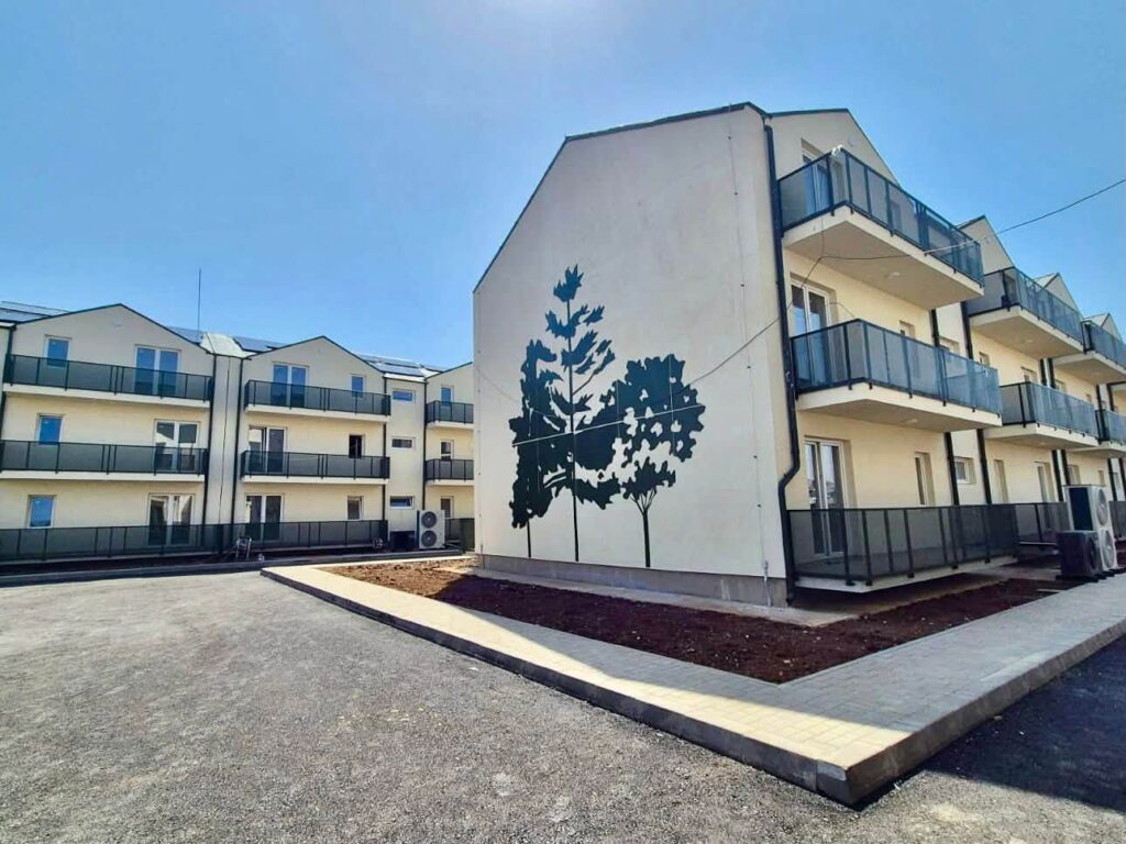 791015079_1392184443097527_3618681433709408379_n - Jurnalul Olteniei – Știri din Craiova și Oltenia Multistory apartment complex with beige walls and glass balconies, a large wall features a dark tree mural.