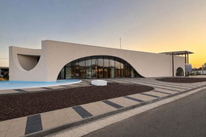 Modern white building with a large curved glass entrance and water feature in front at sunset