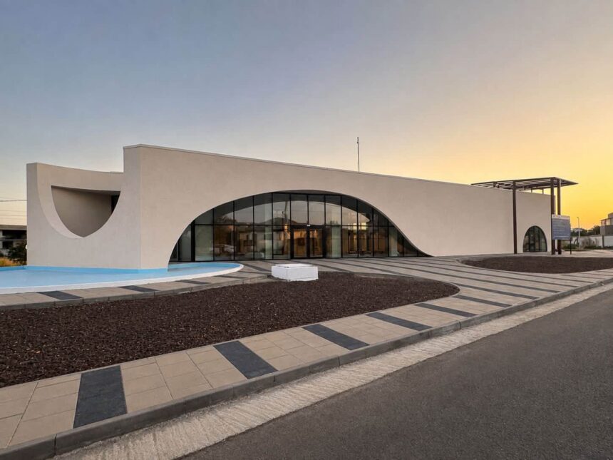 Modern white building with a large curved glass entrance and water feature in front at sunset