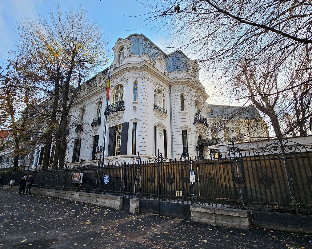 White ornate historic building behind a black iron fence with bare trees framing the scene.]