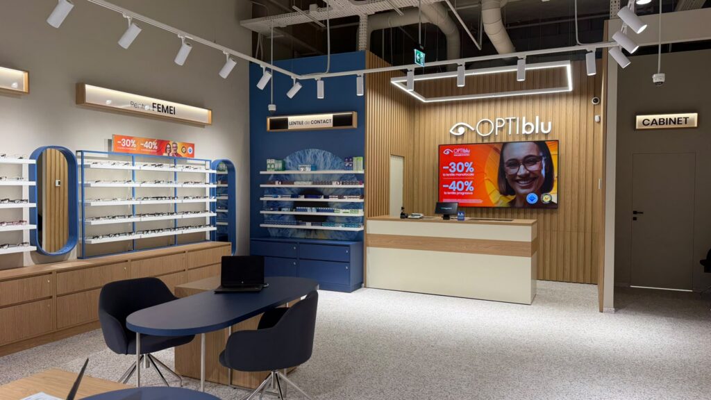 Modern optical shop interior with glasses on blue display racks, wooden cabinets, and a reception desk.