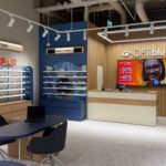Interior of an optical shop with eyeglasses on white-and-blue display shelves and wooden cabinets surrounding a reception desk.