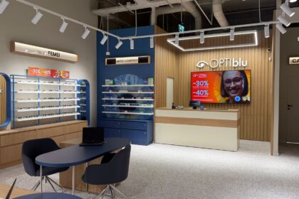 Interior of an optical shop with eyeglasses on white-and-blue display shelves and wooden cabinets surrounding a reception desk.