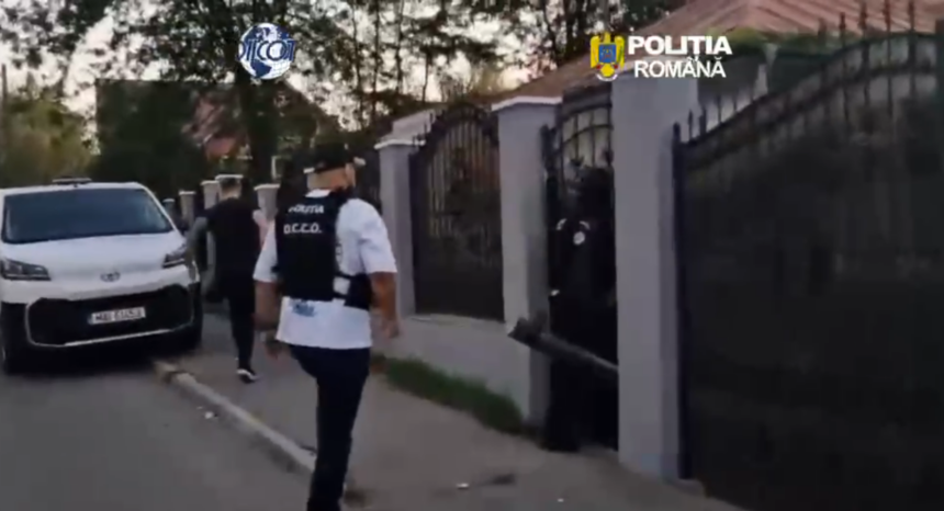 Romanian police officer in a vest walking toward a gated residential entrance beside a white van in a gated neighborhood