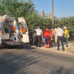 Emergency responders and bystanders surround an ambulance on a residential street, preparing to move a patient on a stretcher short distance from the curb.