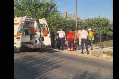 Emergency responders and bystanders surround an ambulance on a residential street, preparing to move a patient on a stretcher short distance from the curb.