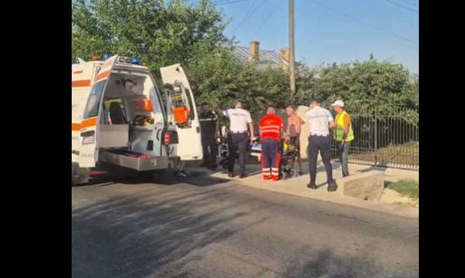 Emergency responders and bystanders surround an ambulance on a residential street, preparing to move a patient on a stretcher short distance from the curb.
