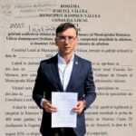 Man in a navy suit holding a white document in front of a large wall with Romanian text, likely at a municipal building.