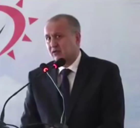 WhatsApp Image 2026-08-05 at 122529 - Jurnalul Olteniei – Știri din Craiova și Oltenia Man in a dark suit delivering a speech at a podium with two red-lit microphones, sun-style logo in the background.