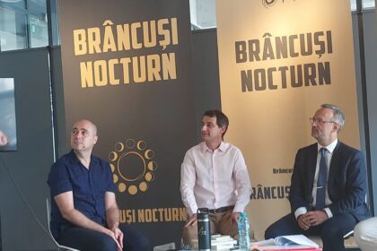Speaker in a white shirt and red striped tie addresses a panel of four men, with large Brâncuși Nocturn banners behind them.