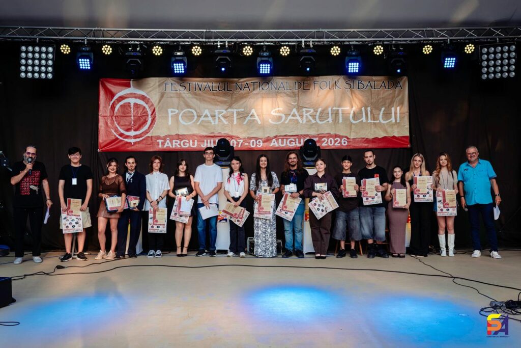 WhatsApp Image 2026-08-10 at 092531 1 - Jurnalul Olteniei – Știri din Craiova și Oltenia Group of young people and a few adults on a stage holding certificates at a national folk festival backdrop.