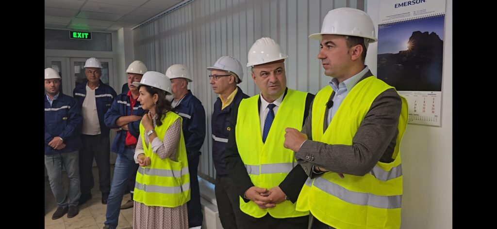 Group of professionals in hard hats and high-visibility vests listening to a briefing in a hallway.