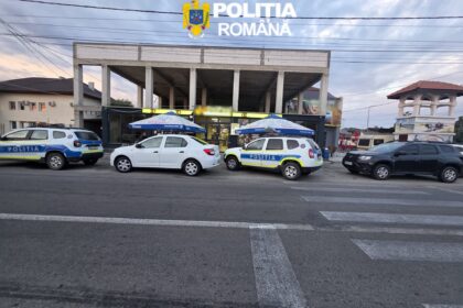 Front view of a Poliția Română building with its crest on a sign, and several police cars parked outside under blue umbrellas.
