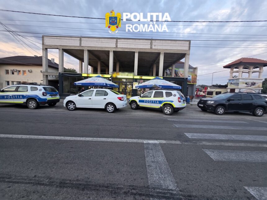 Front view of a Poliția Română building with its crest on a sign, and several police cars parked outside under blue umbrellas.