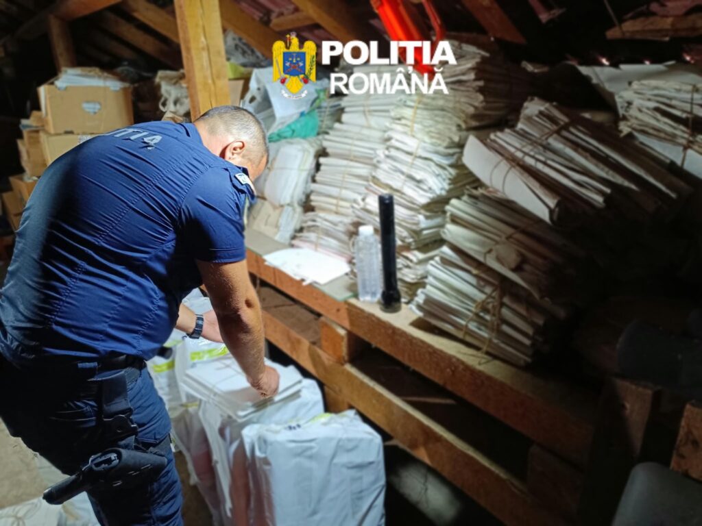 Romanian police officer in a blue uniform examining stacks of papers in a cluttered attic.