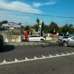 Emergency responders and bystanders at a road collision with a damaged white car and debris on the pavement. wires overhead.