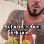 Tattooed shirtless man at the beach holding a box of colorful pastries on sticks; caption in Romanian reads 'Preturi de nebuni pe litoral' (Crazy prices on the coast).