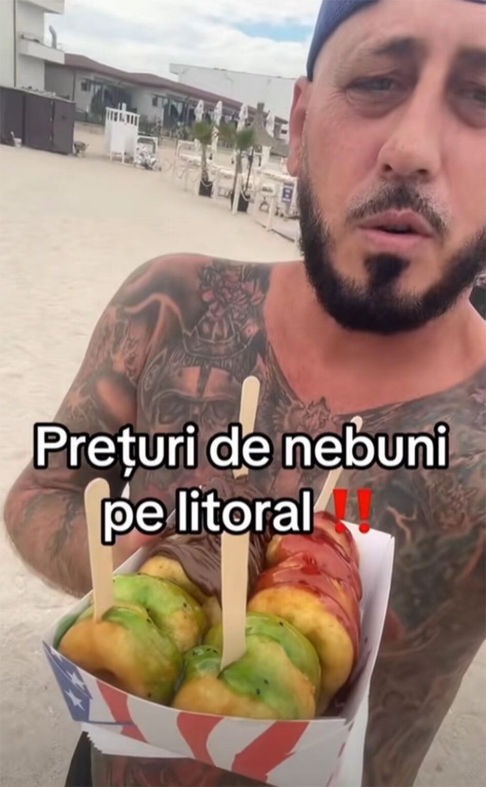 Tattooed shirtless man at the beach holding a box of colorful pastries on sticks; caption in Romanian reads 'Preturi de nebuni pe litoral' (Crazy prices on the coast).
