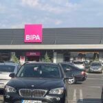 Parking lot in front of a shopping plaza with BIPA and kik storefronts and several cars parked in the foreground
