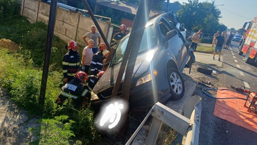Firefighters in red helmets stabilize a blue SUV teetering over a ditch beside a guardrail as onlookers watch the rescue scene by the road.