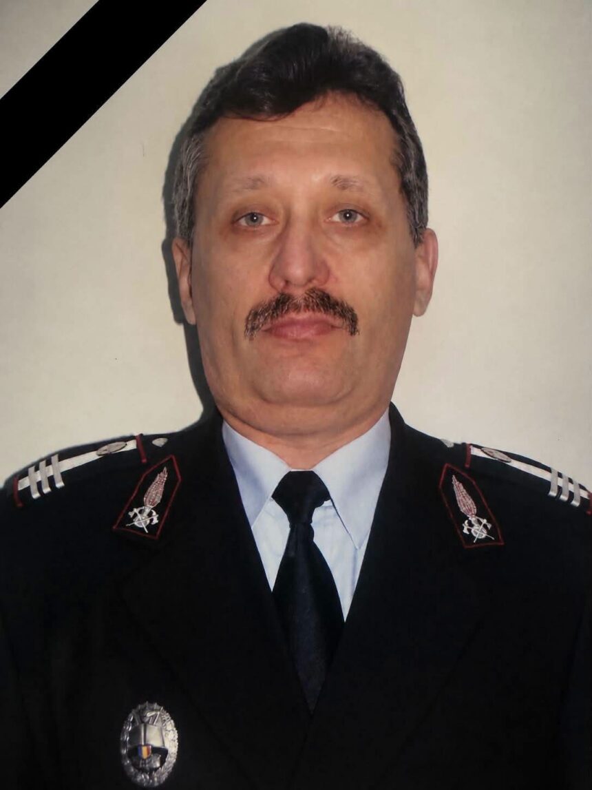Portrait of a male police officer in dress uniform with a mourning black ribbon across the top-left corner, badge visible on chest.