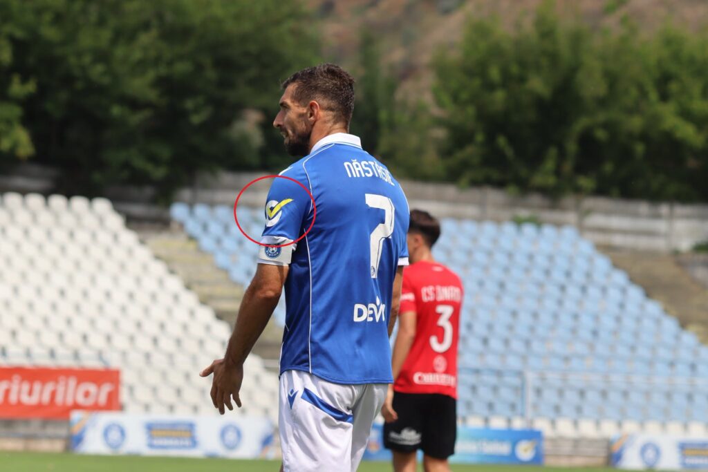 csm insemn electoral 1 - Jurnalul Olteniei – Știri din Craiova și Oltenia Soccer player in a blue jersey with number 7, standing on a field with empty stands in the background; yellow checkmark patch on the sleeve circled.