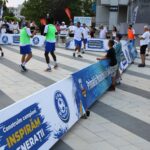 Group of players in a small outdoor futsal court, spectators along the sidelines with blue advertising banners in Romanian.