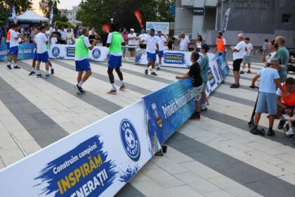 Group of players in a small outdoor futsal court, spectators along the sidelines with blue advertising banners in Romanian.