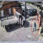 Man steps out of a white delivery truck with its cab door open on a sunny urban street.
