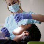 Dental professional in a mask and gloves performing a dental procedure on a patient in a reclining chair.
