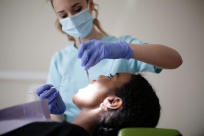 Dental professional in a mask and gloves performing a dental procedure on a patient in a reclining chair.