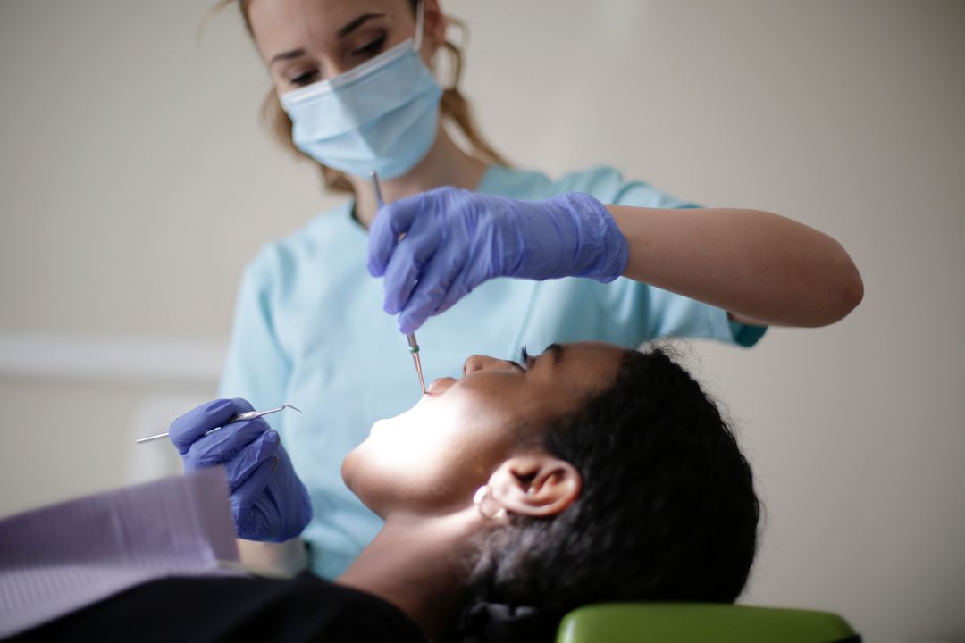 Dental professional in a mask and gloves performing a dental procedure on a patient in a reclining chair.