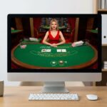 Monitor shows an online baccarat table with a dealer in a red dress; 18+ warning sign sits on the desk beside a mug and clock.