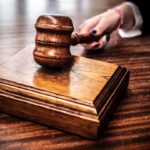 Wooden gavel resting on a polished judge's block on a dark courtroom desk.