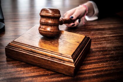 Wooden gavel resting on a polished judge's block on a dark courtroom desk.