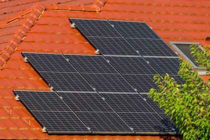 Solar panels mounted on a red tiled roof beside a leafy tree nearby.