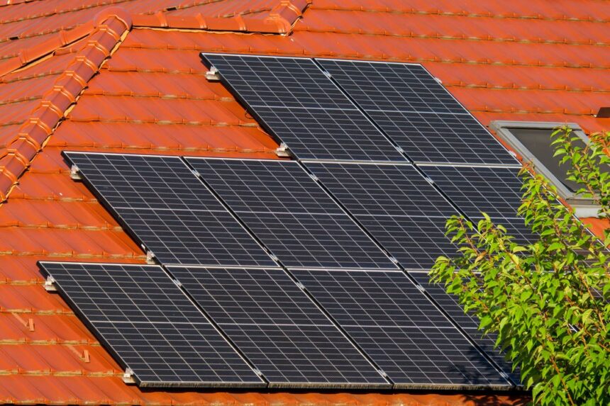 Solar panels mounted on a red tiled roof beside a leafy tree nearby.