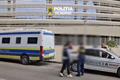 Romanian police van and marked patrol car parked outside a modern building; three blurred individuals stand nearby.