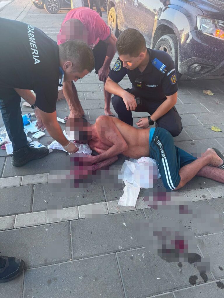 scarisoara WhatsApp Image 2026-08-11 at 101753 - Jurnalul Olteniei – Știri din Craiova și Oltenia Emergency responders kneel beside a severely injured man on a sidewalk after a car crash, with medical supplies nearby.