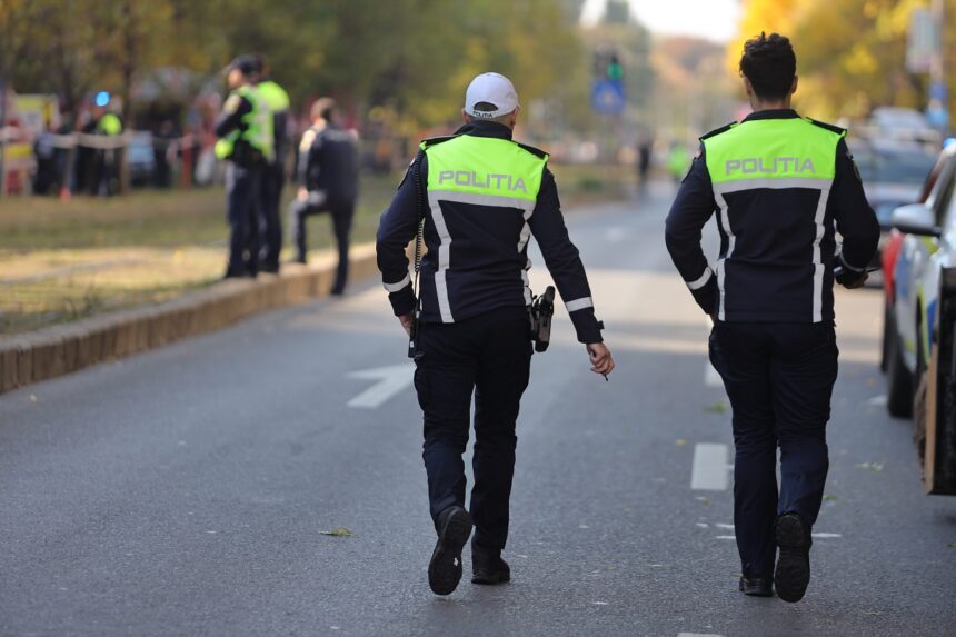 Two police officers in high-visibility jackets walk away down a city street as bystanders stand behind a cordoned area in the background.
